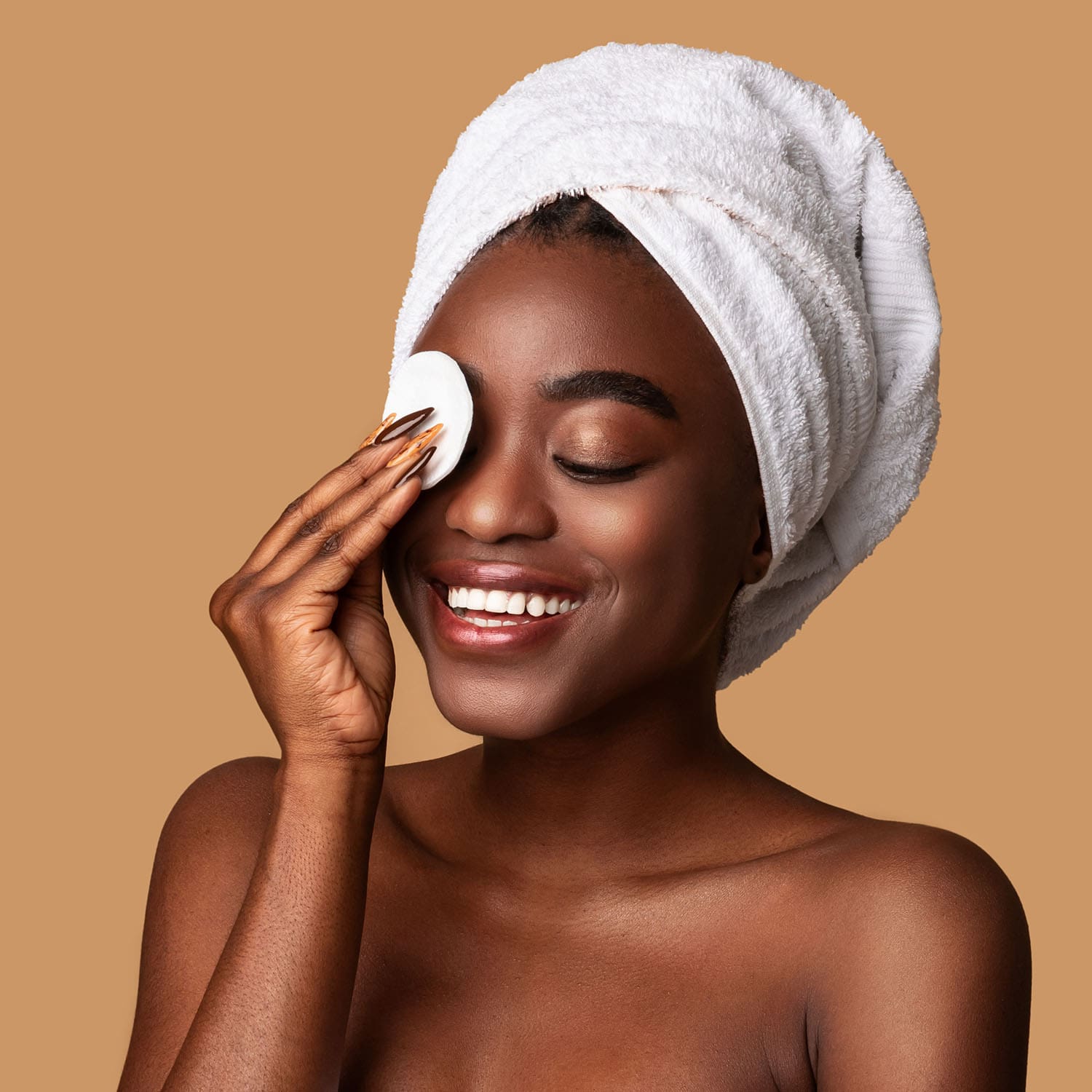 Woman with towel on her head smiling and removing makeup from her eye